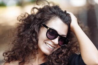 Portrait of a stylish beautiful young curly woman in a black dress and sunglasses