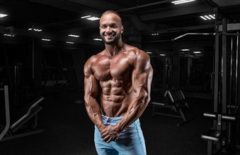 Muscular man in jeans poses in the gym. Sports