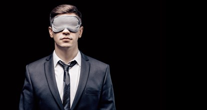 Portrait of a man in a mask for sleeping. He stands against a black wall. Blind business concept. Work during the crisis.