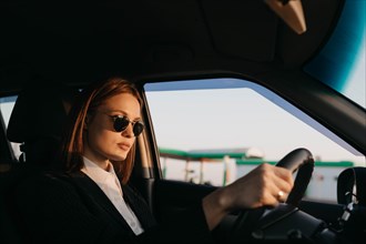 Young beautiful stylish girl driver in a jacket and sunglasses driving a car