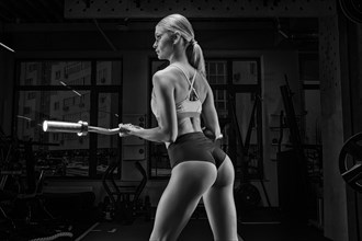 Charming tall athlete posing in the gym with a barbell in her hands. Back view. The concept of sports