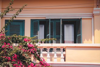 Sunny facade of a pink Mediterranean building with blue shutters and blooming bougainvillea