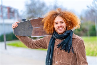 Portrait of a redheaded skater carrying a skate and smiling at camera in an urban park