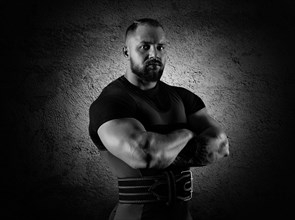 The weightlifter stands in a menacing pose with crossed huge arms and looks at the camera