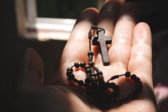 A hand holding a rosary with a cross