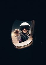 Portrait of a man in a helmet. He looks into the porthole of an airplane and holds out a heart-shaped figure. Travel and insurance concept.