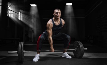 Athlete is standing on his knee and near the bar and is preparing to make a deadlift.