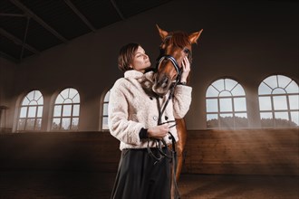 Portrait of a stylish woman hugging a thoroughbred horse. Love and care concept.