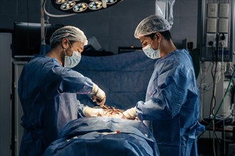 Male surgeons operating on a patient in a hospital operating room. Side view. Scoliosis surgery