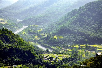 Sunlit valley with winding Sirot river surrounded by lush green mountains and a rural landscape in Manrasa