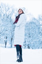 Beautiful girl walks through the snowy forest with a book in her hands. Christmas holidays concept.