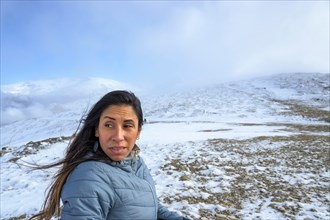 Middle-aged latina woman on a snow-capped mountain in a blizzard