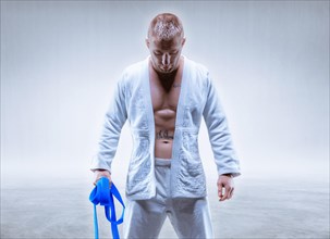 Athlete in a kimono with a blue belt stands with his head down. The concept of karate and judo.
