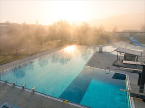 Morning light reflected in the water of a fog-covered swimming pool with slides