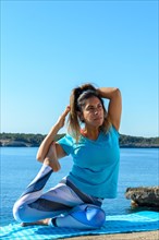 Middle-aged fitness woman outdoors in front of the sea does yoga stretching exercises
