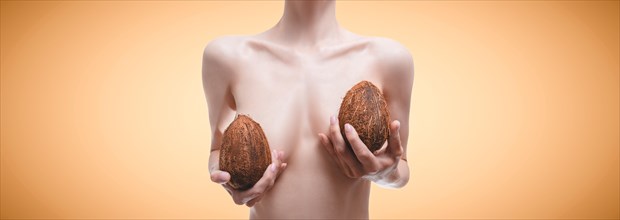 Woman posing in the studio with coconuts in her hands. Plastic surgery concept. Mammalogy. Silicone implants.
