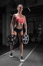 Charming tall athlete posing in the gym with a weight plate. The concept of sports