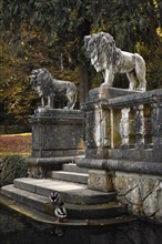 Two lion statues on a stone staircase leading to a small pond
