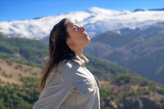 Woman in contemplation facing the sun with snow-capped mountains under a clear sky