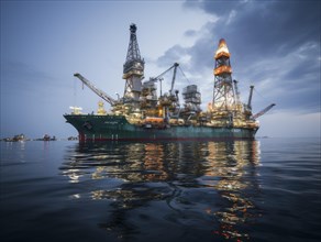 Night view of an offshore drilling ship with bright lights reflecting on ocean waters