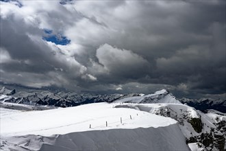 Berlinger Koepfl summit area with snow-covered mountains in the background and dramatic sky