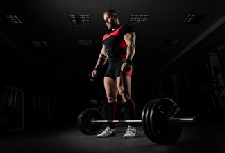 The weightlifter is preparing to perform an exercise called deadlift. He stands directly above the barbell and looks at it