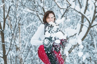 The girl is having fun in the winter forest. She sprinkles everything around with snow. Winter holiday concept. Tourism.