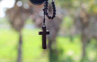 A wooden rosary with a cross hanging in front of a blurred natural background