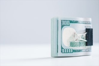 Pack of hundred-dollar bills lies on a white table fastened with a paperclip. The concept of savings during the crisis.