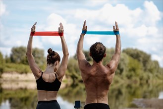 Young athletic couple doing exercise with resistance band on the shore of a lake on a sunny day