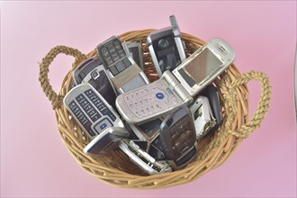 Assortment of old mobile phones piled in a wicker basket with a soft pink background