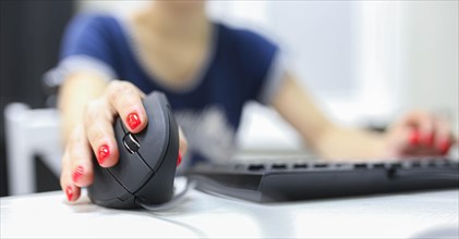Girl's hand uses a vertical ergonomic joystick of a computer mouse. working at the computer