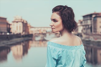 Portrait of a charming girl standing on a bridge in Florence. Arno River. View of the Ponte Vecchio. Tourism concept. Italy.