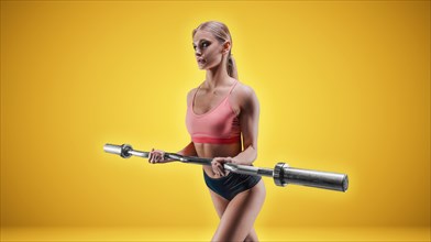 Charming tall athlete posing in the studio on a yellow background with a barbell in her hands. The concept of sports