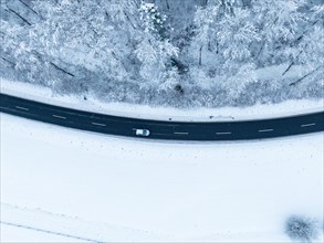A single vehicle driving on a snowy road seen from the air