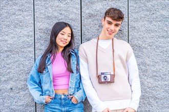 Frontal portrait of two multi-ethnic young couple leaning on a wall carrying a digital camera