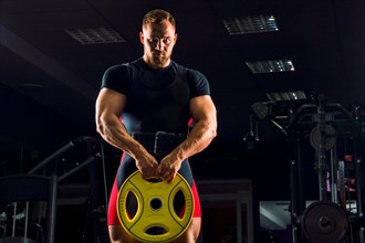 Huge weightlifter stands with a weight in his hands in the gym