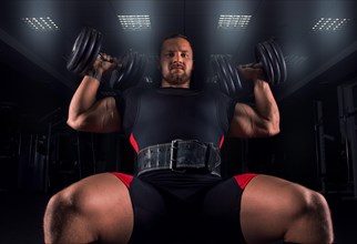 The athlete sits on a bench in the gym and does an exercise called military press