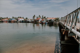 Gentle river by a bridge with tropical houses and boats. Kampot