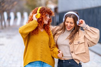 Frontal view of two happy women dancing and listening to music in the street