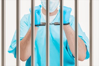 Doctor in handcuffs is standing behind a prison cell. The concept of corruption in medicine.