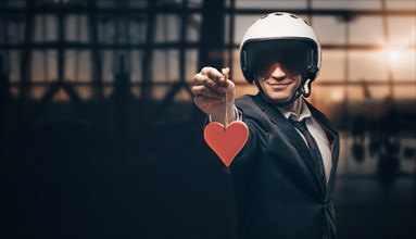 Portrait of a man in a helmet standing in the airport with a red heart in his hands. Travel concept.