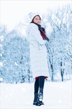 Charming tall woman posing against the backdrop of a snow-covered park with a book in her hands. Christmas holidays concept.