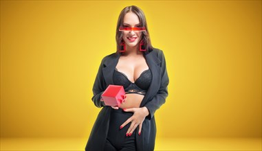 Sexy tall brunette in lingerie holds a red jewelry box. Yellow background. The concept of gifts and congratulations.