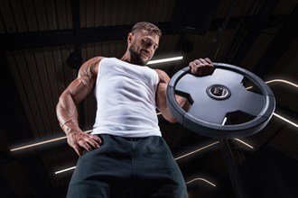 Portrait of a man in a white T-shirt exercising in the gym with barbell discs. Biceps pumping. Fitness and bodybuilding concept.