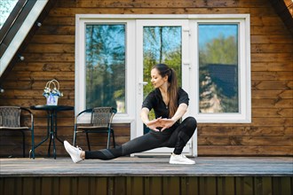 Active adult woman stretching her arms and legs on terrace of her log cabin