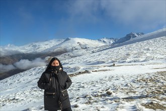 Young latina woman posing with black jacket on snowy mountain very happy