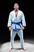 Professional athlete stands in the gym in a kimono with a blue belt. Concept of karate