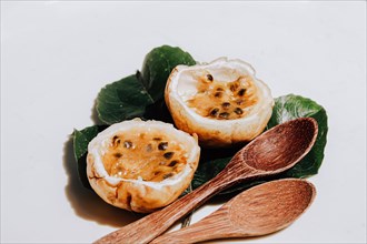 Opened passion fruits beside wooden spoons on a white backdrop
