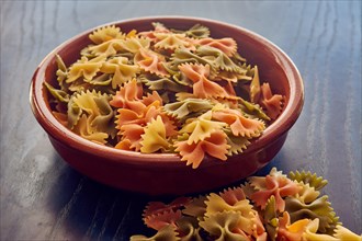 Terracotta bowl full of bow-tie pasta sitting on a wooden table